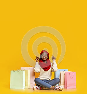 Amazed black girl with purchases pointing up at empty space