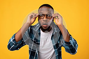 Amazed Black Man Looking At Camera Through Glasses, Yellow Background