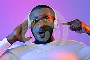 Amazed black man wearing sunglasses using wireless headphones