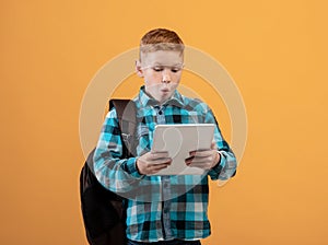 Amazed boy schooler with backpack using digital tablet