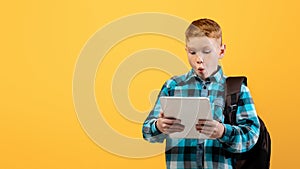 Amazed boy schooler with backpack using digital tablet