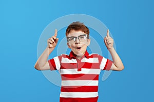 Amazed boy wearing striped red shirt and eyeglasses, pointing up with opened mouth while having idea