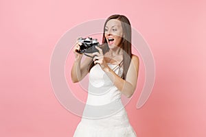 Amazed bride woman in wedding dress taking pictures on retro vintage photo camera choosing staff, photographer