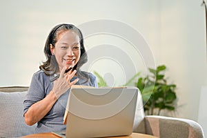 Amazed and cheerful Asian-aged retired woman looking at her laptop screen