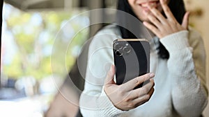 Amazed and cheerful young Asian woman using her smartphone while relaxing in the coffee shop