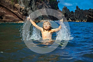 Amazed child playing and splashing in the sea. Kid having fun outdoors. Summer vacation and healthy family lifestyle