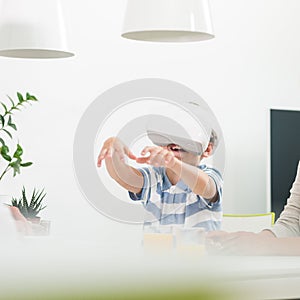 Amazed child using virtual reality headsets trying to grab unexisting virtual objects while sitting at the dinner table.