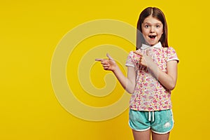 Amazed cute girl kid, points away with both forefingers, shows blank space