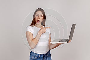 Amazed emotional woman pointing laptop screen and looking at camera with shocked expression.