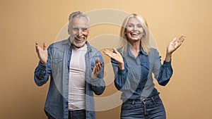 Amazed excited elderly man and woman gesturing on beige background