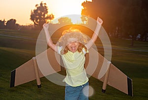 Amazed excited kid playing with toy plane on sunny golden sunset sky background outside on grassy summer hill. Dreaming