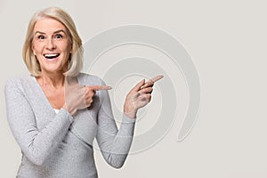 Amazed excited mature woman pointing at copyspace isolated on background