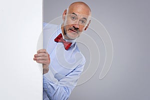 Amazed face man wearing bow tie and looking out of white board while standing at isolated background