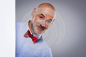 Amazed face man wearing bow tie and looking out of white board while standing at isolated background