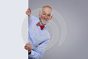 Amazed face man wearing bow tie and looking out of white board while standing at isolated background