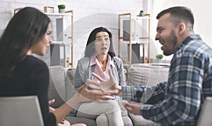 Amazed family therapist looking at mad couple arguing at session