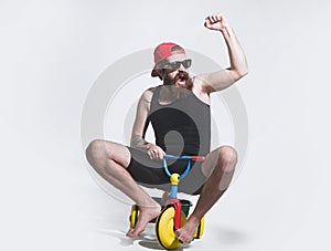 Amazed funny bicycle rider, excited man on colorful bicycle toy in sunglasses, cap. Guy riding childs tricycle.