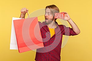 Amazed funny shopper guy holding Sale word, looking big eyes surprised expression at shopping bags