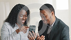 Amazed happy businessman and businesswoman look at smartphone receiving SMS message reading good news. Excited overjoyed