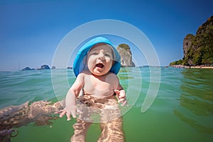 Amazed infant baby of seven months bathes in the sea for the first time. Sunny day, dad holds the baby. Only hands of man