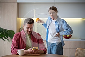 Amazed jealous shocked woman stands behind back peeping in man husband smartphone on kitchen at home