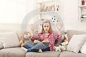 Amazed little girl with book and her favorite toys at home