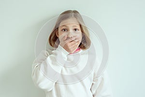 Amazed little girl with widely opend eyes shut her mouth with hand