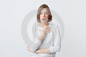 Amazed lovely young woman in longsleeve standing with opened mouth and hands folded isolated over white background Feels shocked