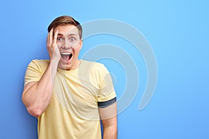 amazed man in basic clothing screaming in surprise or delight and closing face with hand isolated over yellow background