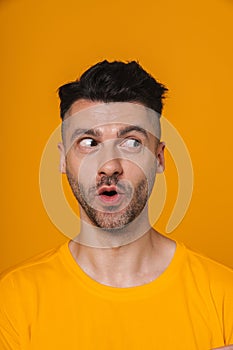 Amazed man looking away while standing isolated over yellow background