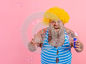 Amazed man with yellow wig in head play with bubbles soap