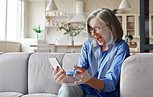 Amazed mature older woman reading message on smart phone at home.