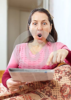 Amazed mature woman looks newspaper