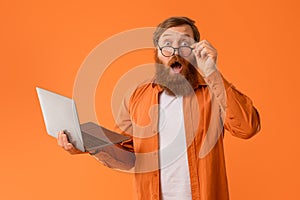 Amazed redhaired bearded guy holds laptop looking at camera, studio