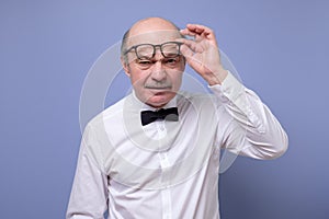 Amazed senior man looking at camera through glasses having some doubts