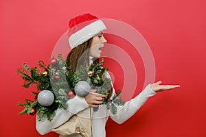 Amazed shocked young woman holding bouquet of spruce branches presenting with palm workspace area copy space, wearing white