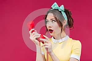 Amazed shocked young woman talking on telephone with red receive