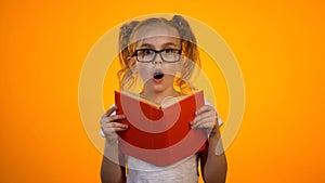 Amazed smart girl in glasses holding book and looking to cam, interesting story