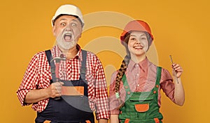 amazed teen child and grandfather carpenter in helmet on yellow background
