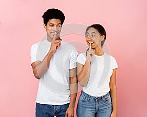 Amazed teen couple make silence sign, keep forefingers on lips