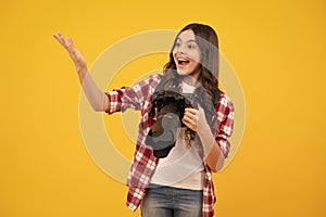 Amazed teenager girl with dslr professional photo camera with big photo lens. Child photographer isoalted on yellow