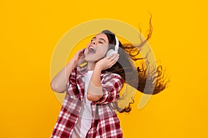 Amazed teenager. Teenager child girl in headphones listening music, wearing stylish casual outfit isolated over yellow