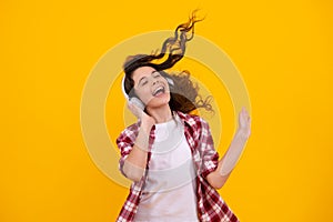 Amazed teenager. Teenager child girl in headphones listening music, wearing stylish casual outfit isolated over yellow