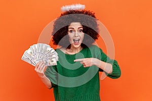 Amazed woman with Afro hairstyle wearing green casual style sweater and nimb over head holding big