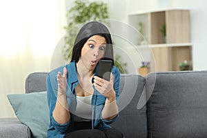 Amazed woman checking cell phone content at home