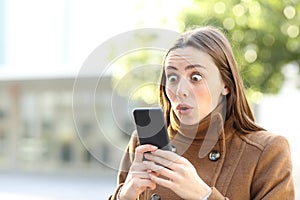 Amazed woman checking mobile phone in winter