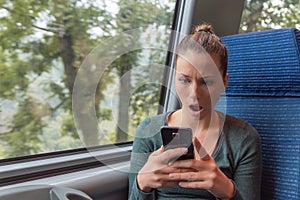 Amazed woman checking smartphone in the street after receiving a shocking news on a train journey