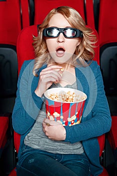 Amazed woman in glasses eating popcorn