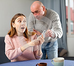 Amazed woman trying to don't give away her phone to her jealous husband