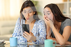 Amazed women checking smart phone at home